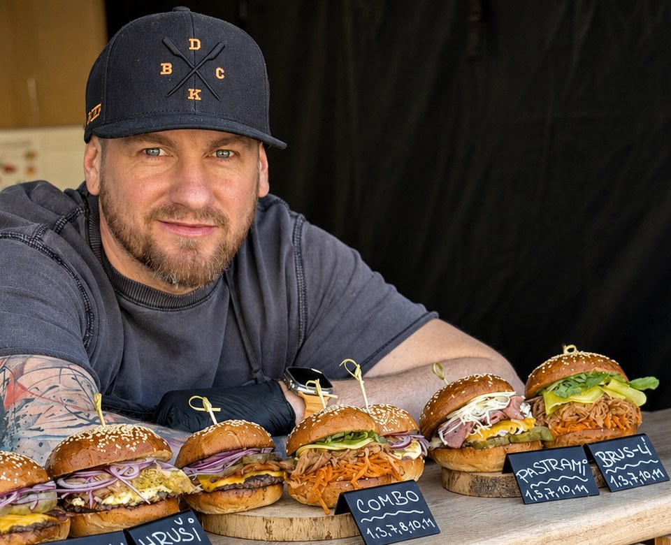Michal Neuman, zakladatel Dycky Burger, za pultem foodtrucku s pěti burgery na dřevěných prkénkách